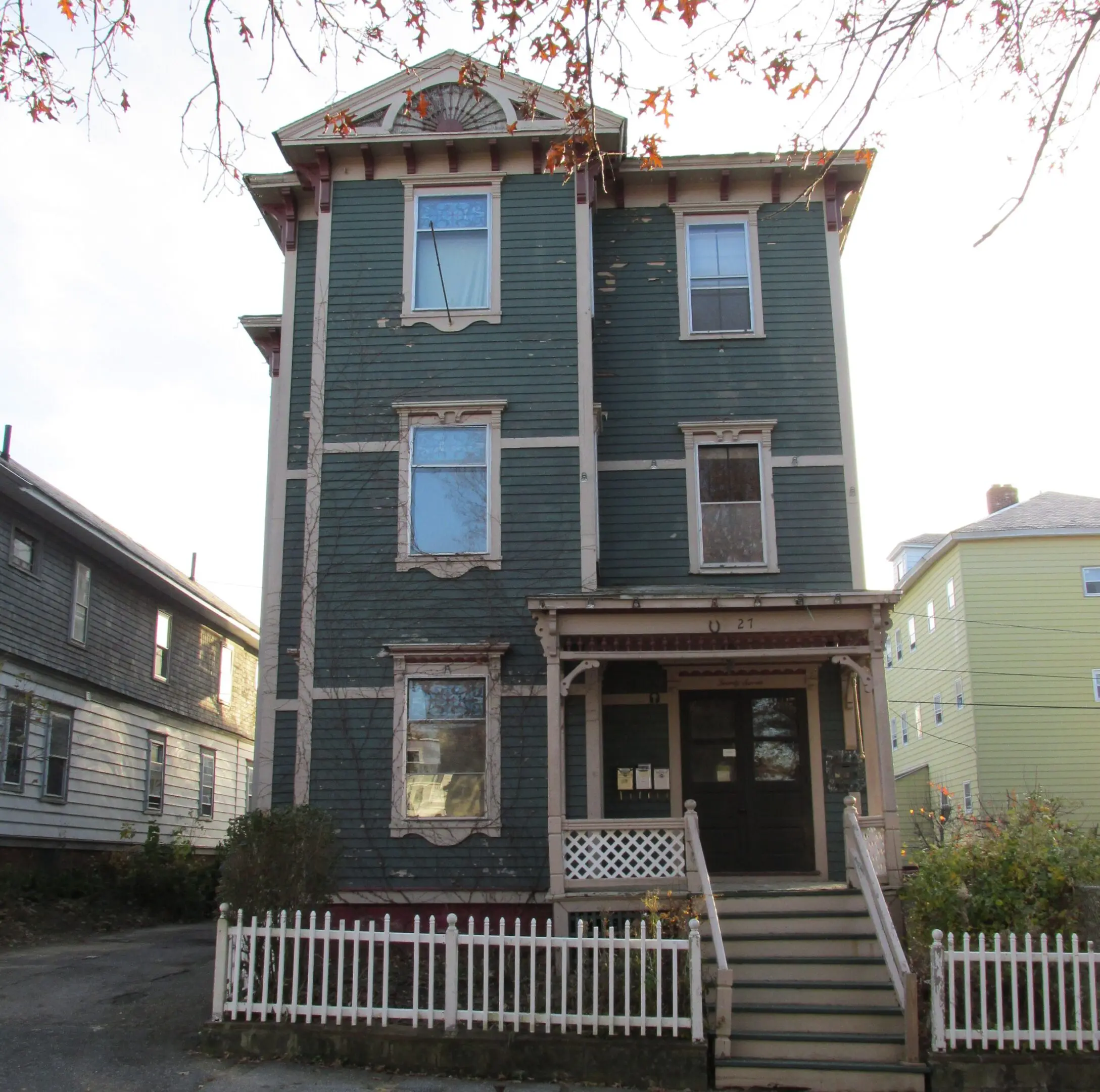 Three-story residential building with a small front porch and white fence.
