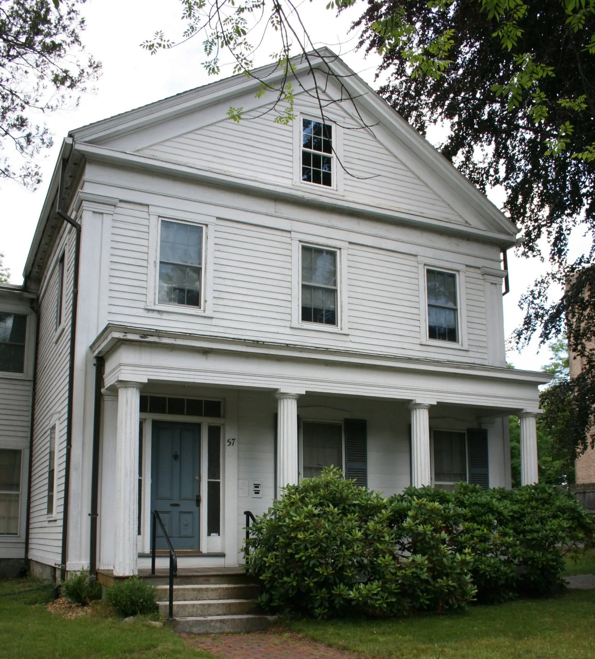 Large white colonial house with a porch and green shrubbery.